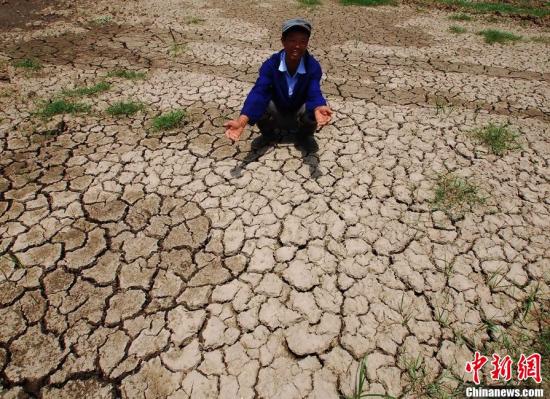 資料圖：5月20日，江西省九江縣城子鎮(zhèn)，一農(nóng)民蹲在因干旱無(wú)法栽種的稻田上。胡國(guó)林 攝