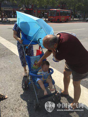 7月31日，西安街頭兩位老人為孩子遮陽(yáng)防曬。（張宏芳 攝）